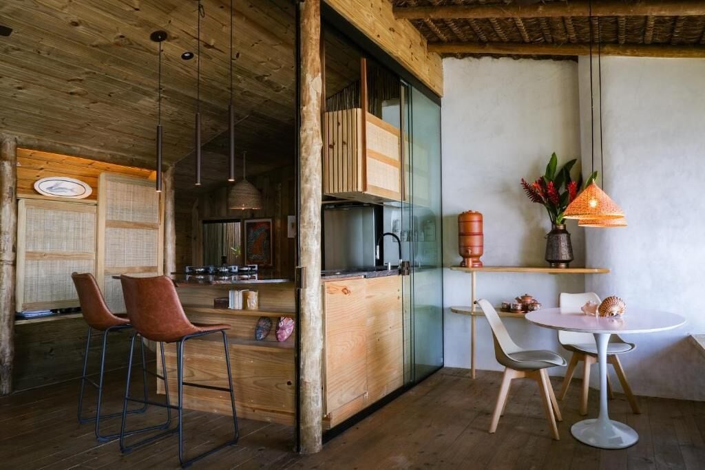 A rustic kitchen with wooden cabinets, a refrigerator, and a dining area with a round table and chairs.