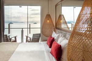 Een hotelkamer met een groot bed, twee rode kussens en uitzicht op zee door een glazen deur.
