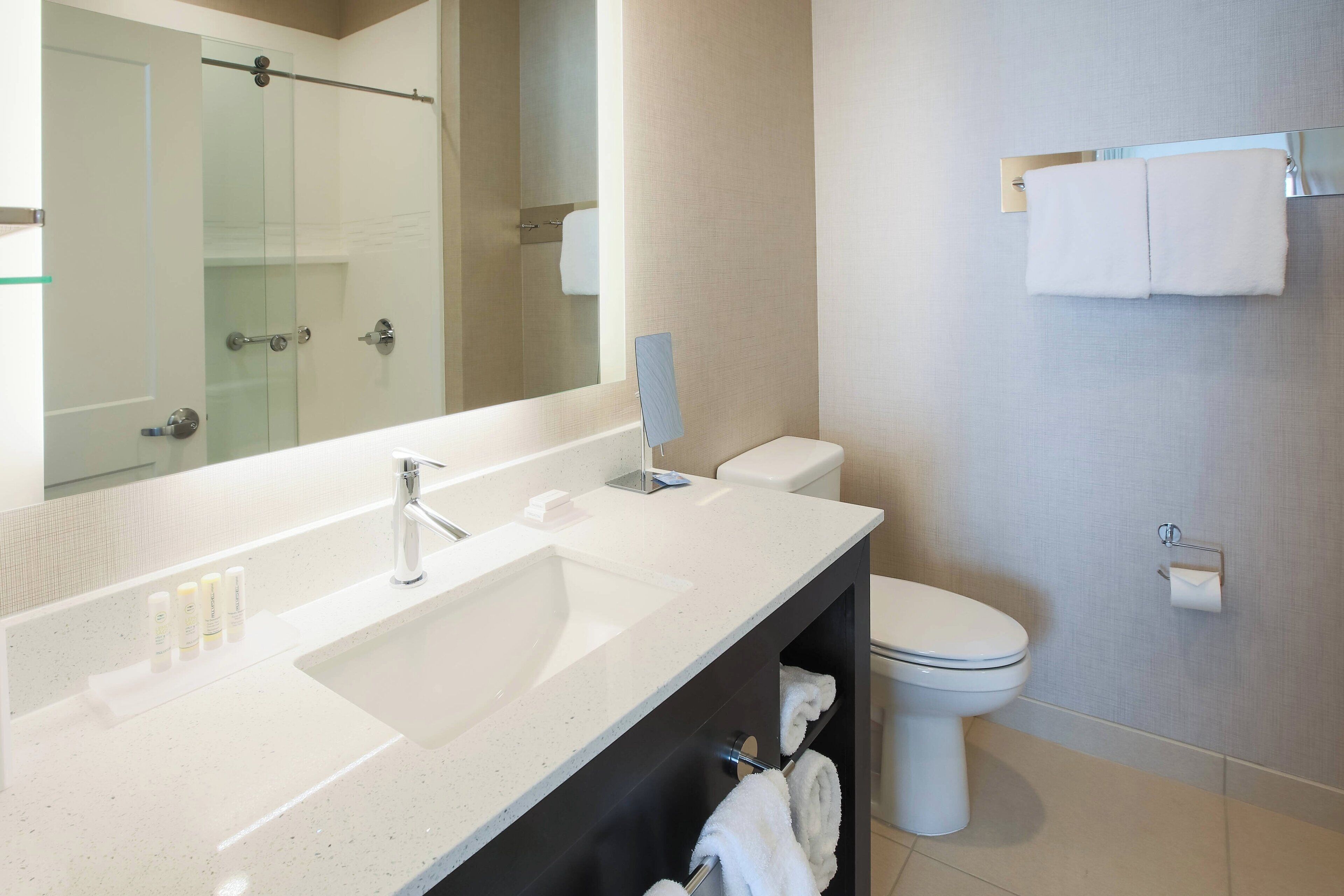 A modern bathroom with a large mirror, a sink, a toilet, and a glass shower enclosure.