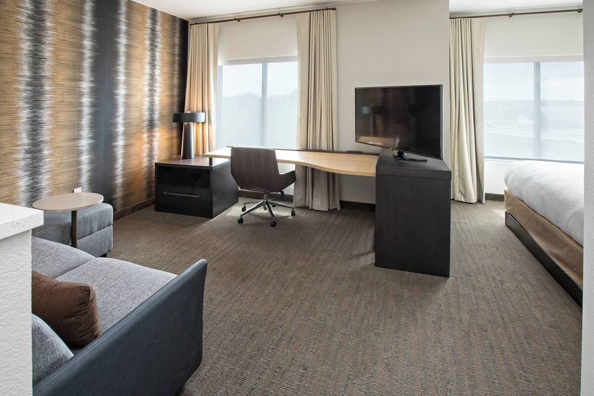Ein Hotelzimmer mit einem Bett, einem Schreibtisch mit Stuhl, einem Fernseher, einem kleinen Tisch und einem Sofa.