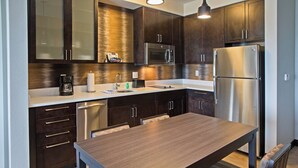 A modern kitchen with dark wood cabinets, stainless steel appliances, and a wooden dining table. - Residence Inn by Marriott Louisville East/Oxmoor (Louisville)