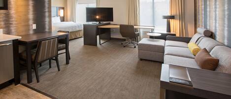 Quarto de hotel com cama, escrivaninha com televisão, sofá e área de jantar.