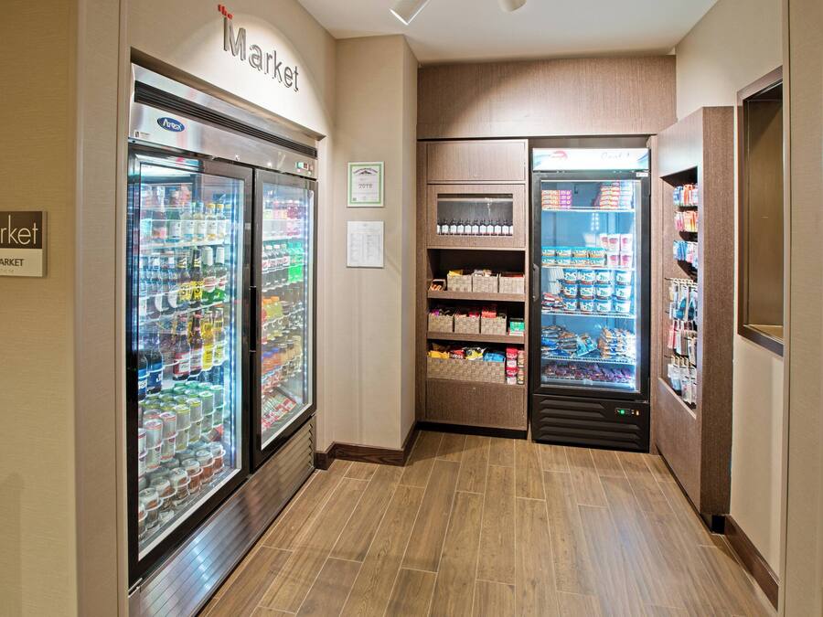 A corridor with refrigerated display cases stocked with beverages and snacks, wooden flooring, and a sign indicating a market area.