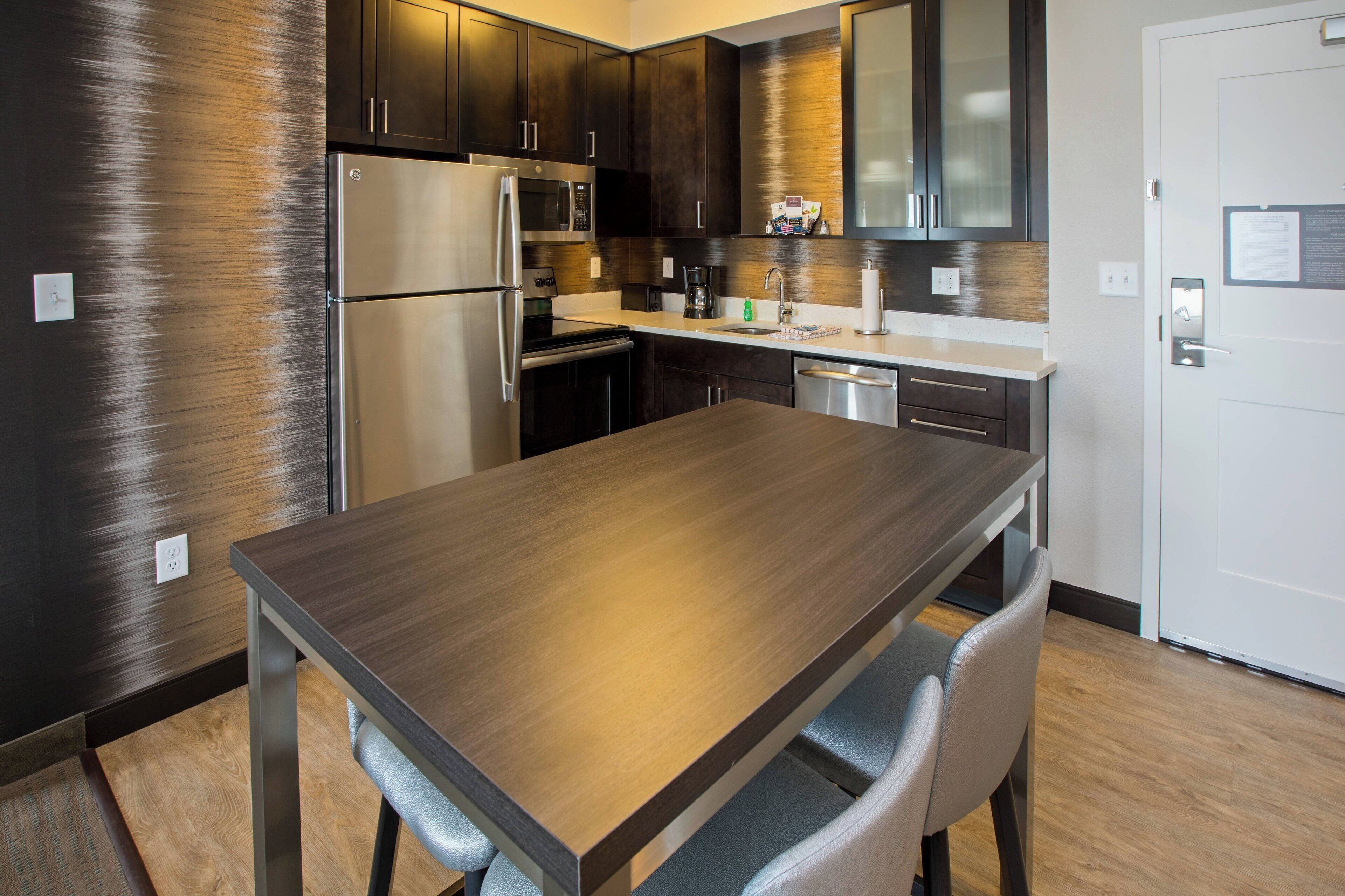 A modern kitchen with stainless steel appliances, dark wooden cabinets, and a wooden dining table with chairs.