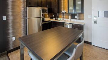 A modern kitchen with stainless steel appliances, dark wooden cabinets, and a wooden dining table with chairs.