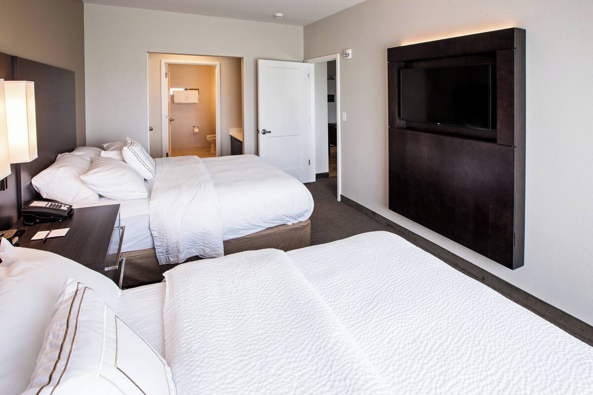 Ein Hotelzimmer mit zwei Betten, einem an der Wand montierten Fernseher und einem Schreibtisch mit Telefon und Notizblock.