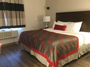 A hotel room with a large bed, a bedside lamp, a window with curtains, and a wall-mounted air conditioner. - Ramada by Wyndham Bronx Terminal (Bronx)