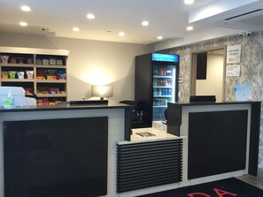 A reception area with a counter, a wall-mounted TV, a beverage fridge, and a sign indicating complimentary breakfast. - Ramada by Wyndham Bronx Terminal (Bronx)
