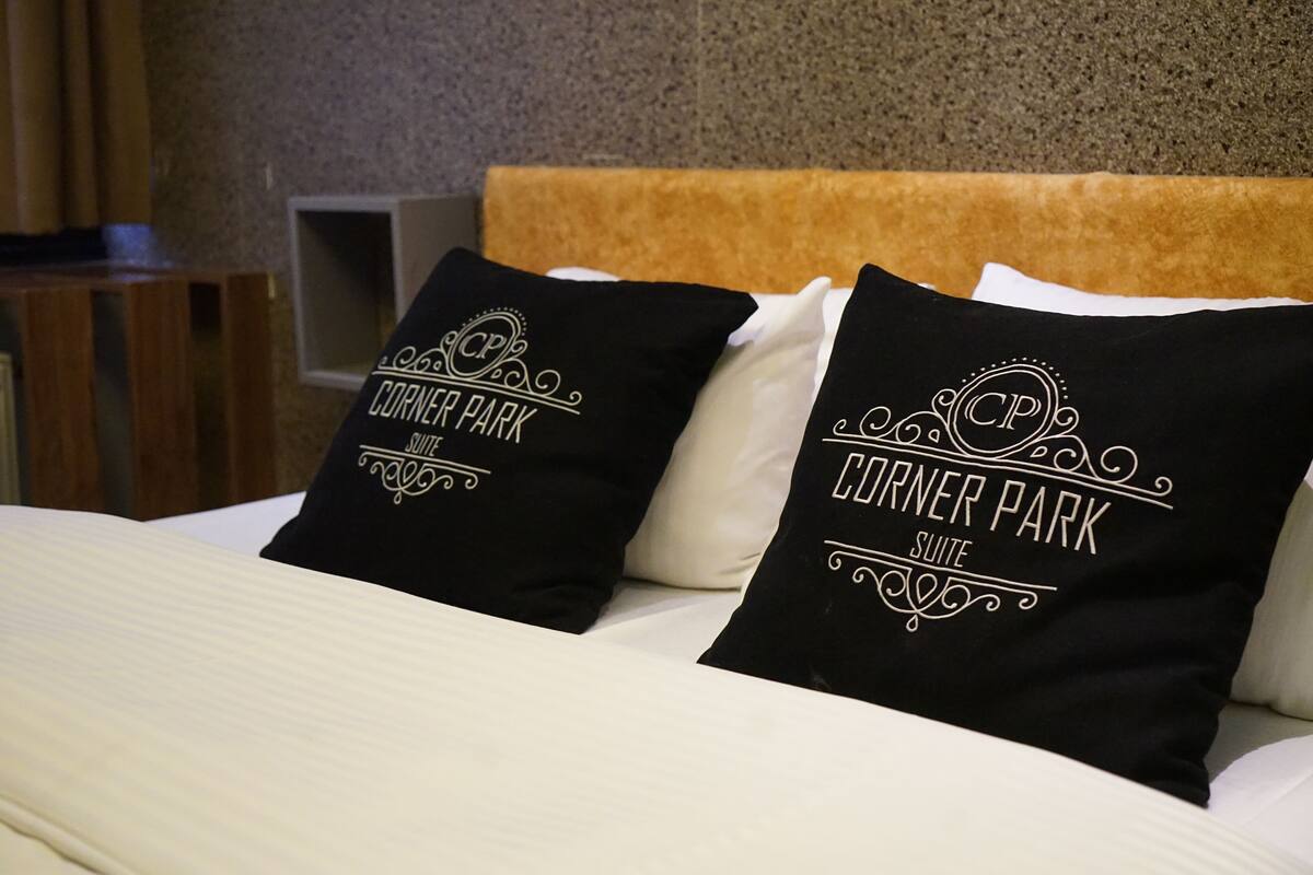 A bed with two black pillows and a white pillow, all featuring the text "Corner Park Suite".