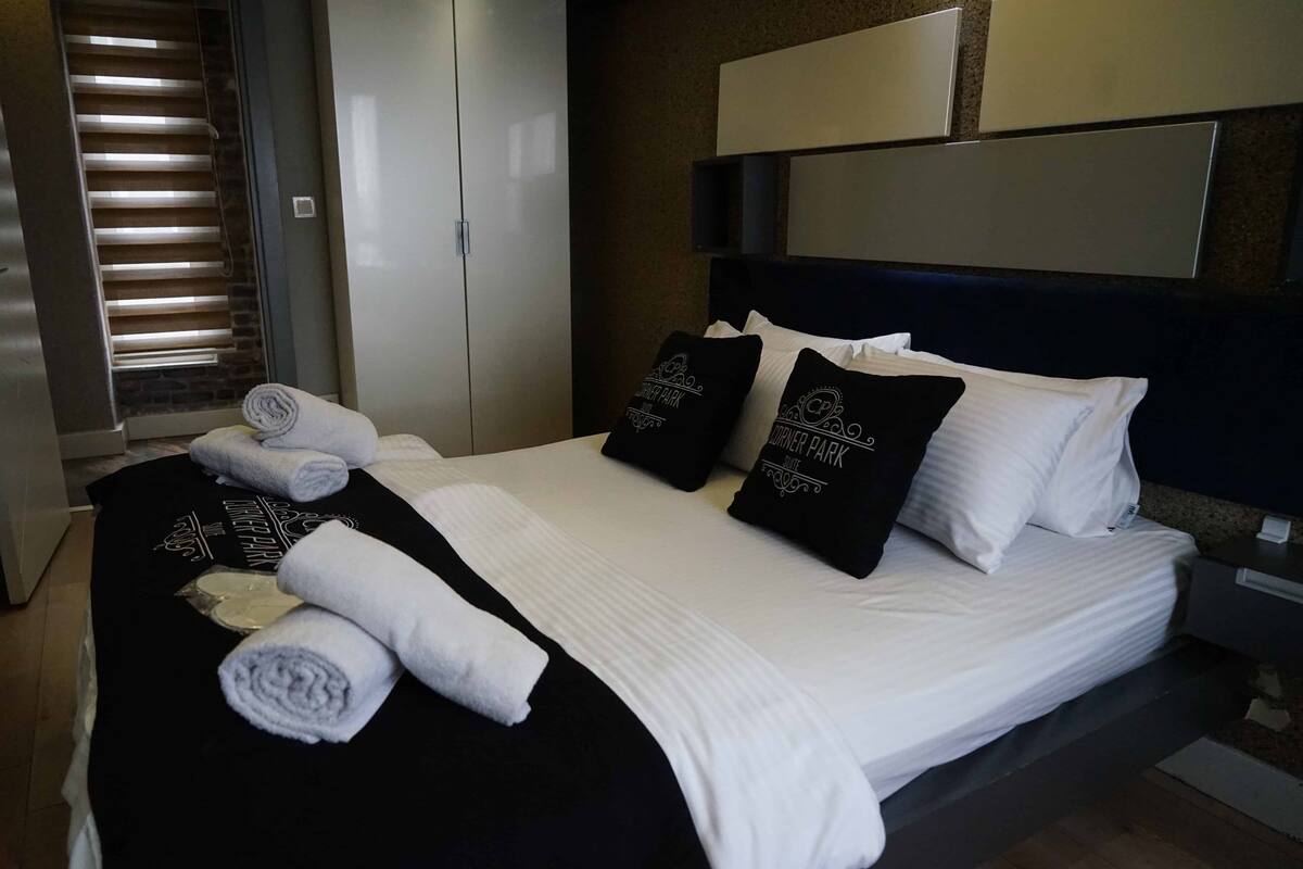 A neatly made bed with white linens, black and white pillows, and rolled towels.