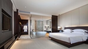Una habitación de hotel moderna con una cama grande, un baño independiente con bañera, un vestidor y un televisor de pantalla plana.
