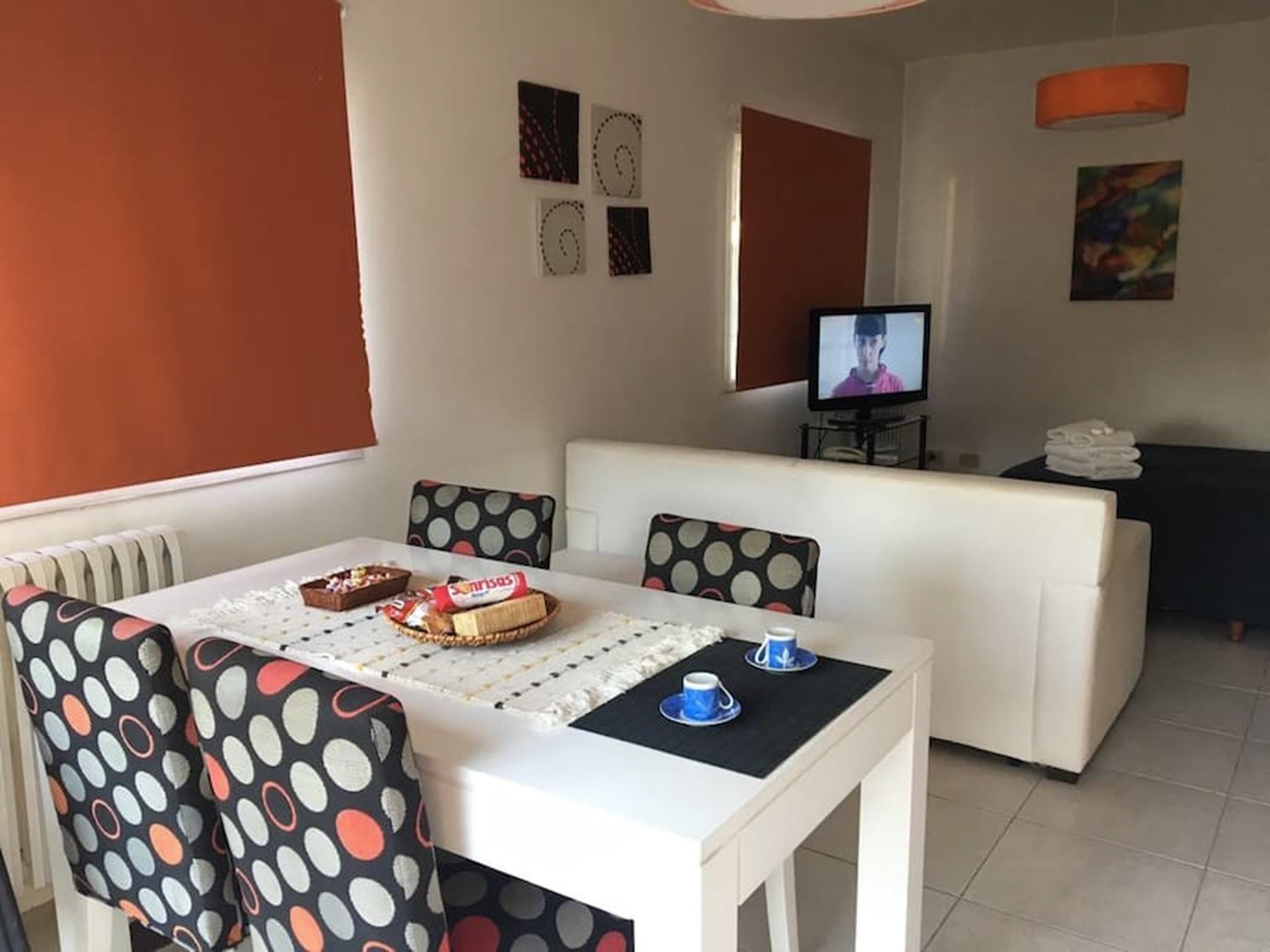 Una sala de estar moderna con un sofá blanco, una mesa de comedor con mantel de lunares y un televisor sobre un mueble.