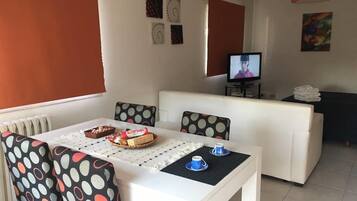 Una sala de estar moderna con un sofá blanco, una mesa de comedor con mantel de lunares y un televisor sobre un mueble.