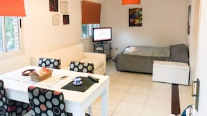 A modern living room with a white sofa, a dining table with chairs, a TV, and a bed. - Apartamento en Country Pilar Frutales (Pilar)