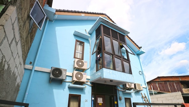 Un edificio azul con varias unidades de aire acondicionado, el número 26 visible en la puerta y una entrada con portón.