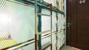 Una habitación con un separador de malla metálica, una puerta de madera con un adorno con forma de corazón y una cama amarilla con un cojín a rayas.
