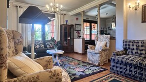 A living room with floral-patterned furniture, a chandelier, and a view of the outside. - Posada Río Cubas (Ribamontan al Monte)