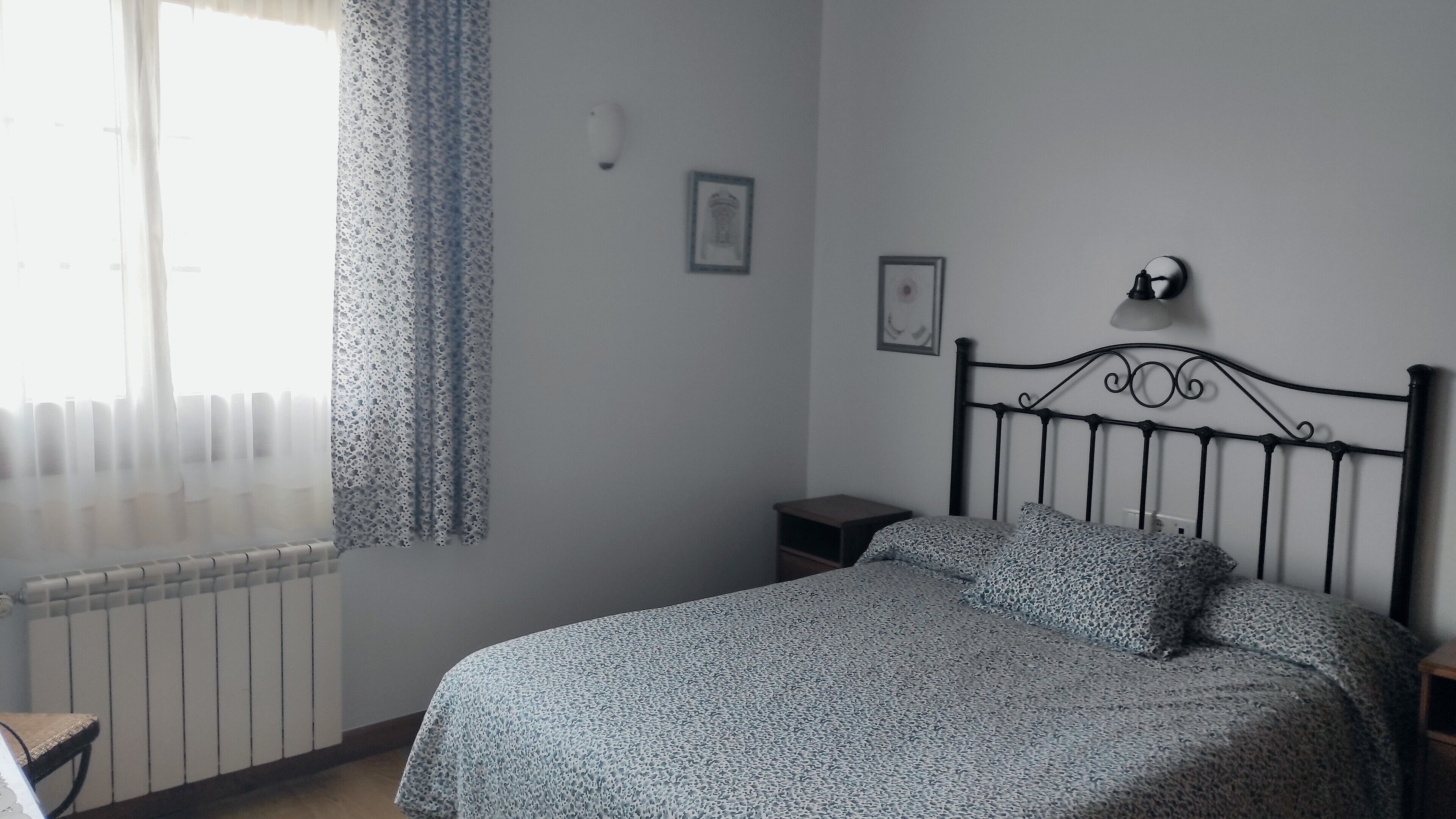 A bedroom with a bed, a nightstand, a radiator, and a window with curtains.