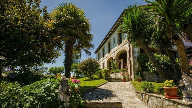A stone staircase leading to a building with a garden and palm trees. - Posada Río Cubas (Ribamontan al Monte)