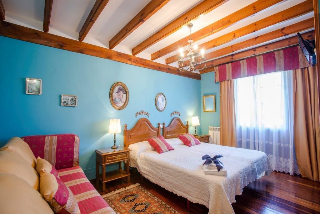 A bedroom with a wooden ceiling, two beds with white linens, a red sofa, and a patterned rug.