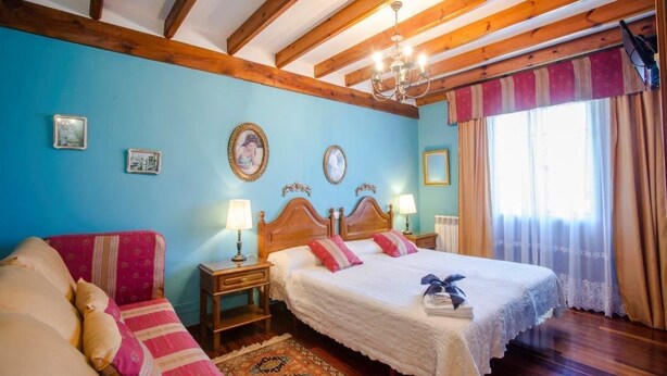 Un dormitorio con techo de madera, dos camas con ropa blanca, un sofá rojo y una alfombra estampada.