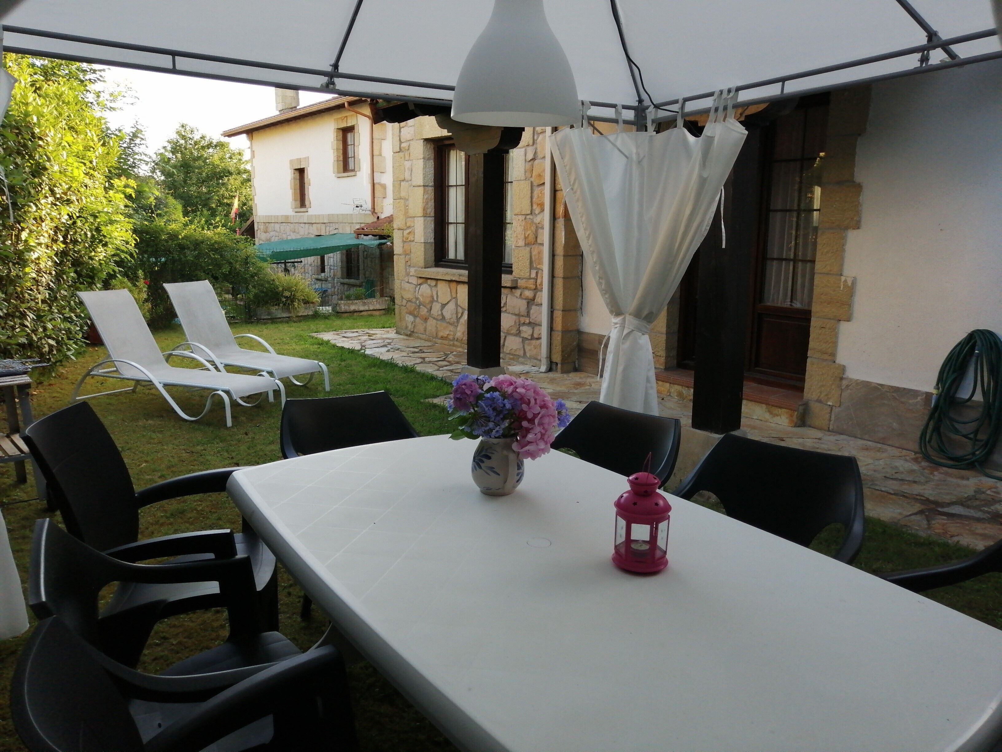 A covered patio area with a table, chairs, a vase of flowers, and a lantern.