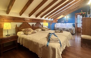 A bedroom with two beds, wooden beams, a nightstand, a lamp, a dresser, and a chair.