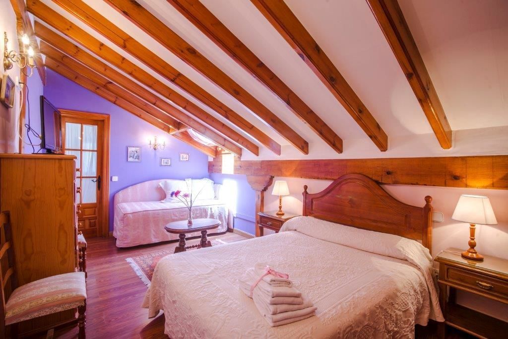 Un dormitorio con una cama grande, una cama más pequeña, vigas de madera, un escritorio y una silla.