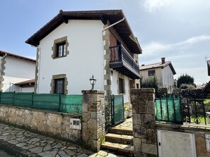 A two-story house with a stone facade, a balcony, and a green fence.