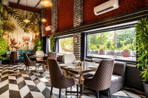 A restaurant with a checkered floor, quilted chairs, a mural of flowers, and a view of greenery outside. - Oriental Palace Resorts (Udaipur)