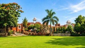 A large, well-maintained lawn with a stone structure and a palm tree in the center. - Oriental Palace Resorts (Udaipur)