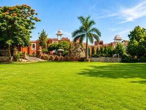A large, well-maintained lawn with a stone structure and a palm tree in the center. - Oriental Palace Resorts (Udaipur)