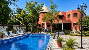 A swimming pool with lounge chairs, a fountain, and a building with a dome and arches. - Oriental Palace Resorts (Udaipur)