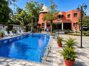 A swimming pool with lounge chairs, a fountain, and a building with a dome and arches. - Oriental Palace Resorts (Udaipur)