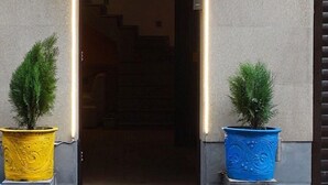 Una entrada de edificio con un camino iluminado que lleva a una puerta, flanqueada por dos macetas.