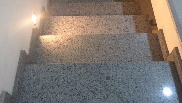 Una escalera de granito con barandales, que lleva a un rellano con una lámpara.