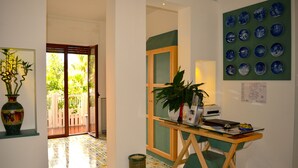 A room with a desk, a potted plant, a wall with blue plates, and a door leading to an outdoor area.