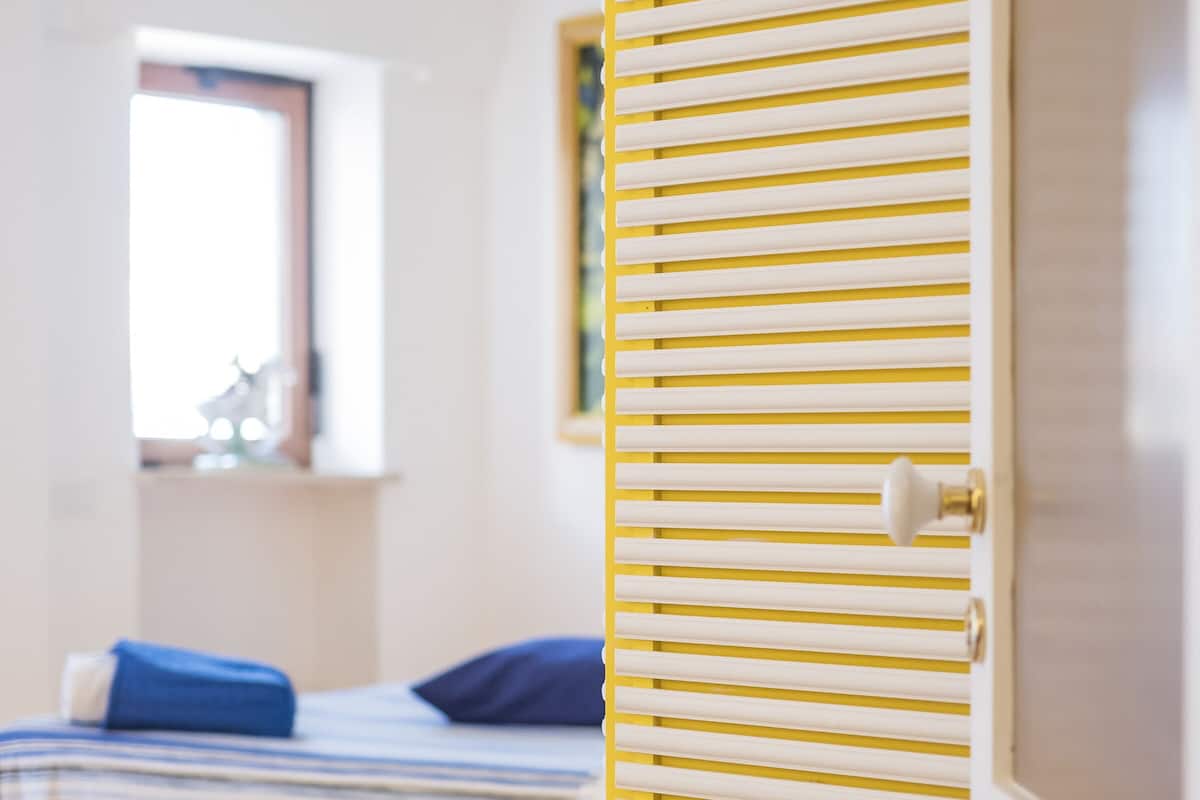 A room with a bed, a window, and a door with horizontal blinds.