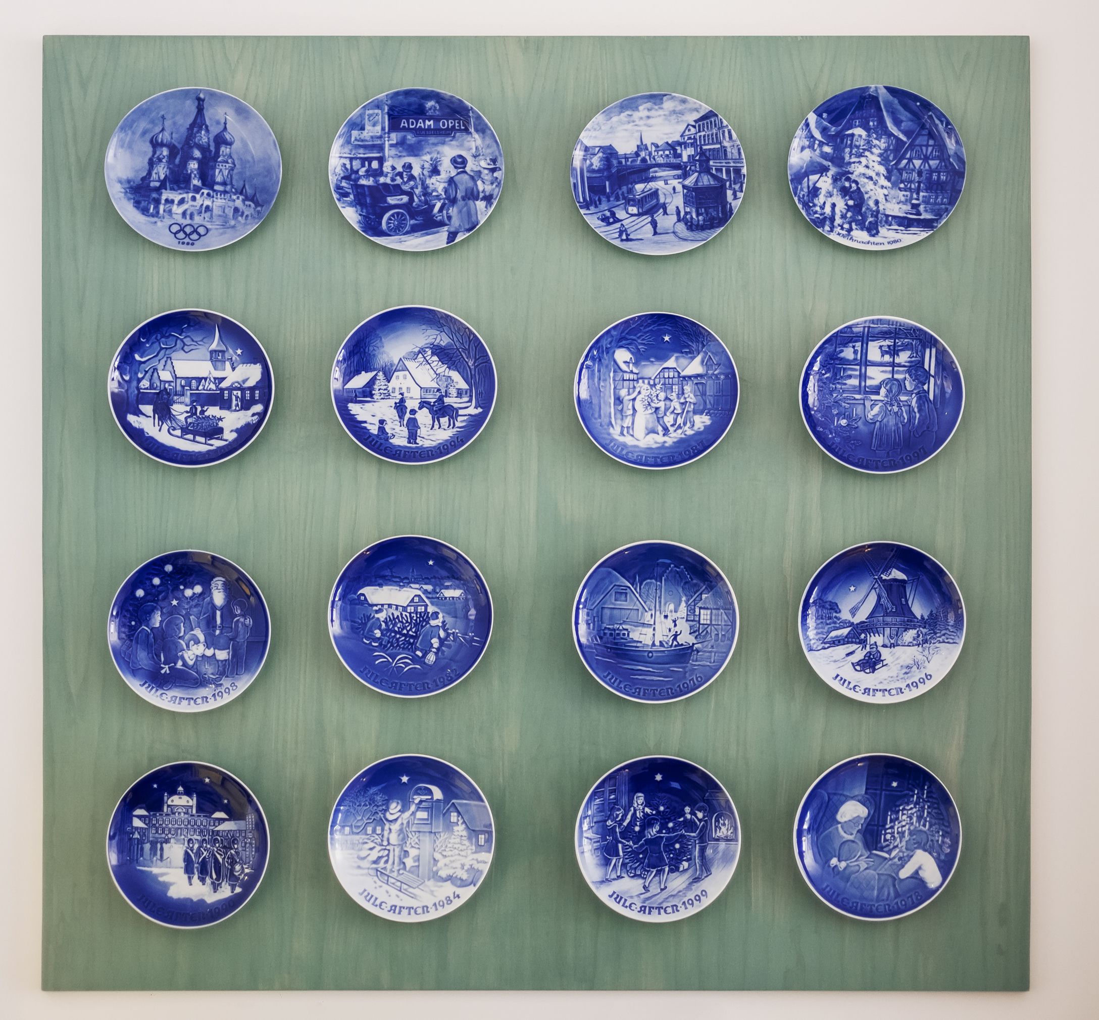 A collection of blue and white ceramic plates with various historical and cultural scenes, arranged in a grid on a green background.