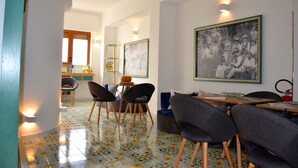 A dining area with a tiled floor, chairs, a table, and a large framed picture on the wall.