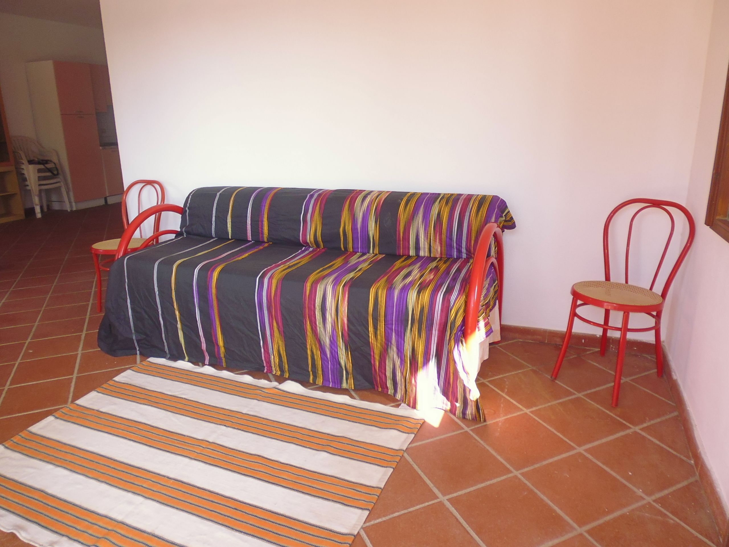 A small living area with a sofa, two red chairs, and a striped rug.