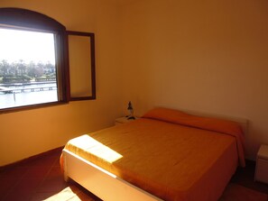 A bedroom with a bed, a nightstand, a lamp, and a window with a view of a park and a body of water. - Residence La Bricola Laghi di Sibari (Cassano allo Ionio)
