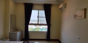 A hotel room with a large window, a bedside table, a mirror, and an air conditioning unit on the wall. - New CityView Safe Home 5min to Downtown (Phnom Penh)
