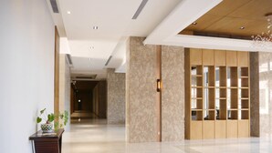 Un hall d’hôtel moderne avec un sol en marbre, un comptoir d’accueil, une cloison en bois dotée d’étagères et une plante sur le côté gauche.