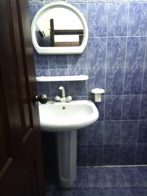 A bathroom with a pedestal sink, a mirror above it, and blue-tiled walls. - MerryDay Inn (Lahore)
