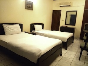 A hotel room with two single beds, a bedside table with a lamp, a TV, and an air conditioning unit on the wall. - MerryDay Inn (Lahore)