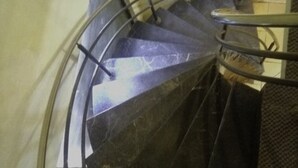 En spiralformet trappe med metalgelændere og en mørk, struktureret væg.