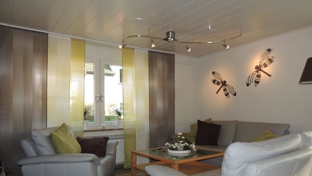A modern living room with a sofa, armchairs, a coffee table, and decorative wall art. - Pension-Neuenrade (Neuenrade)