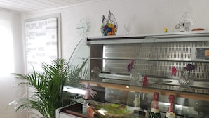 A bar area with a glass display case containing bottles, a potted plant, and decorative items. - Pension-Neuenrade (Neuenrade)