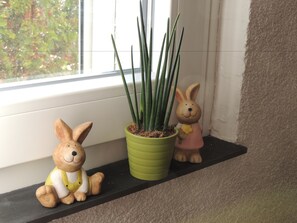 Deux statuettes de lapins en céramique sont posées sur une étagère, à côté d’une plante en pot.